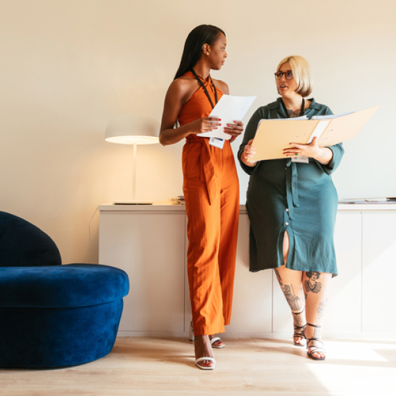 Two women standing and reading papers to each other in a business setting